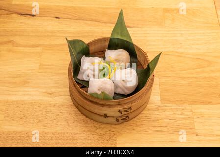 Pork and chives dumplings. Kao stuffed with steamed pork on banana leaves in traditional wooden container Stock Photo