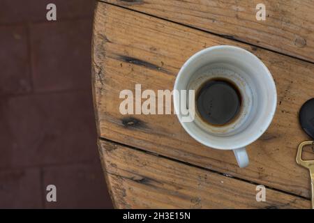 Top view of an empty Espresso coffee cup, placed on a wooden table next to a golden key Stock Photo