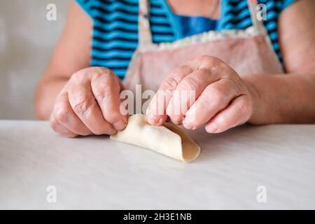 Grandma prepares a dish of dough; only her hands are visible. Blurred background Stock Photo