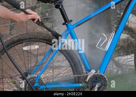 Man cleaning blue bicycle using high pressure washer Stock Photo
