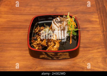 Beef cooked in a Chinese restaurant with sauteed mushrooms and bamboo, bean sprouts, white rice and teriyaki sauce on a traditional wooden plate Stock Photo