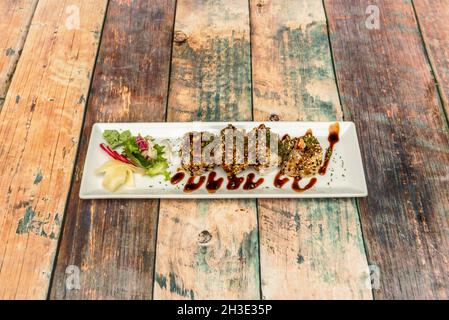 Sushi uramaki dragon roll stuffed with fried prawns in tempura with soy sauce, nori algae, ginseng and Japanese wasabi on wooden table Stock Photo