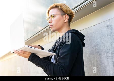 Concentrated young male freelancer typing on modern netbook while standing on street in city during online work Stock Photo
