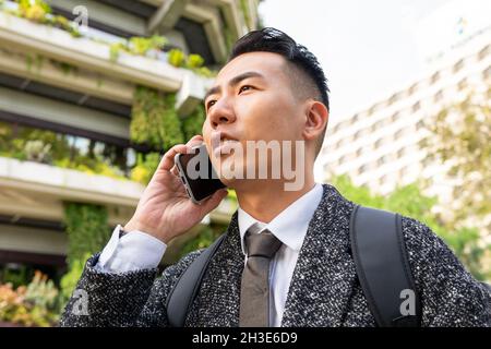 Young ethnic male entrepreneur with tie looking forward while speaking on cellphone in town Stock Photo