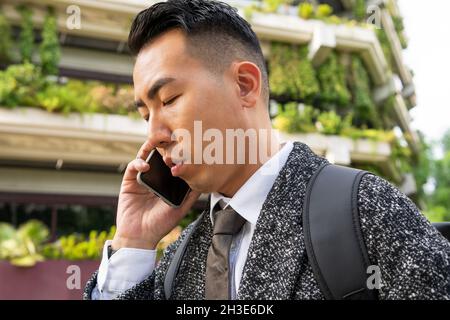 Young ethnic male entrepreneur with tie looking forward while speaking on cellphone in town Stock Photo