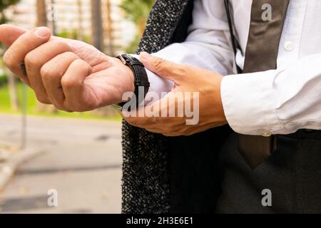 Crop anonymous well dressed male executive in wristwatch touching wrist on roadway in city on blurred background Stock Photo