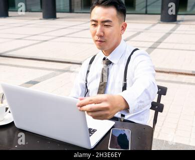 Young ethnic male entrepreneur surfing internet on laptop while sitting at urban cafeteria table Stock Photo