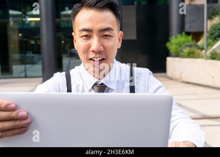 Young ethnic male entrepreneur surfing internet on laptop while sitting at urban cafeteria table Stock Photo