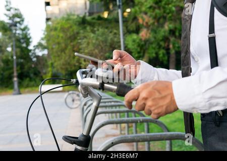 Crop anonymous male manager in formal wear with bicycle using sharing application on cellphone on urban pavement Stock Photo