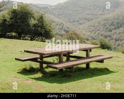 Hilly area covered with grass with wooden table and bench located against cloudy sky in countryside on summer day in nature Stock Photo