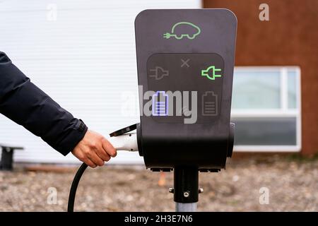 Crop anonymous tourist in warm clothes charging electric vehicle in modern station standing near display with various indicators Stock Photo