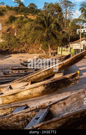 Row of aged wooden boats moored on sandy beach of ocean against green tropical plants on São Tomé and Príncipe island in sunny day Stock Photo