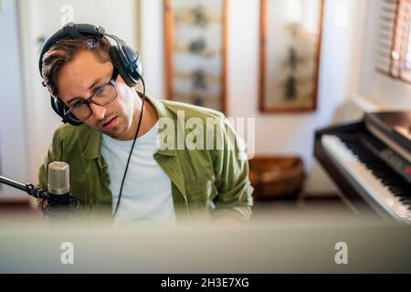 From above concentrated guy with headphones sitting at table and working on computer Stock Photo