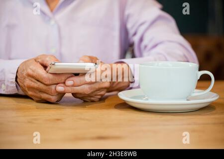 Midsection of senior woman using smart phone at table in cafe || Model approval available Stock Photo