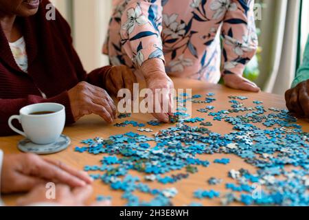 Hands of two diverse senior women and african american male friend doing puzzles. socializing with friends at home. || Model approval available Stock Photo