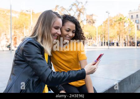 Happy young multiethnic female friends smiling and taking selfie on street Stock Photo