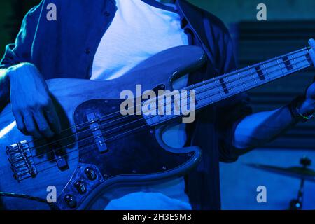 Crop anonymous male guitarist playing electric guitar in club with neon blue lights Stock Photo