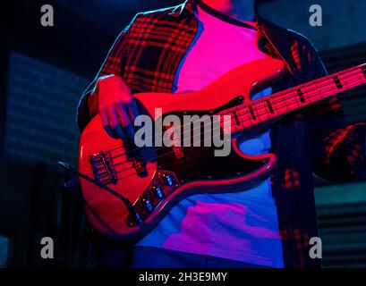 Crop anonymous male guitarist playing electric guitar in club with neon purple and blue lights Stock Photo
