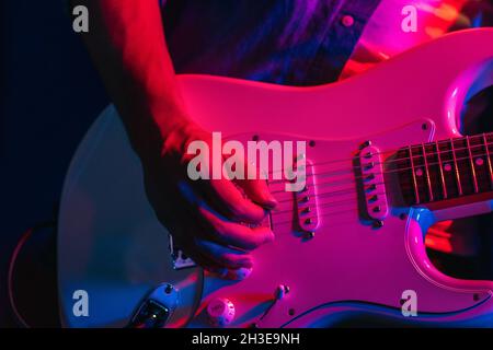Crop anonymous male guitarist playing electric guitar in club with neon purple and blue lights Stock Photo