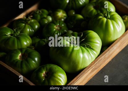 Box full of unripe green tomatoes placed on black table at harvest season Stock Photo