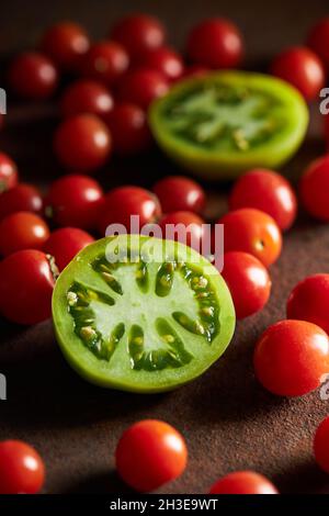 Sliced of unripe berry of Solanum lycopersicum plant with scattered cherry tomatoes Stock Photo
