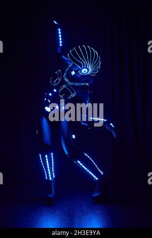 Faceless person in contemporary glowing suit of space cyborg with neon illumination and helmet standing on black background in dark studio Stock Photo