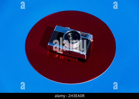 From above retro photo camera placed on metallic red circle on blue background Stock Photo