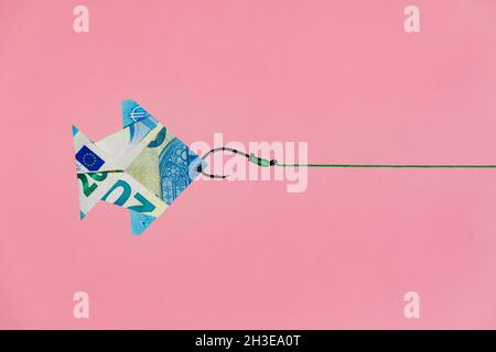 Hook on line pulling origami fish shaped euro banknote as concept of wealth and money earning against pink background Stock Photo