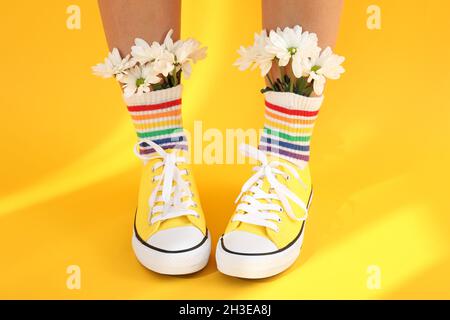 Female legs in rainbow socks with flowers and in sneakers on yellow background Stock Photo