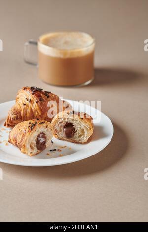 From above of sweet croissants with chocolate placed on white plate near blurred cup of coffee Stock Photo
