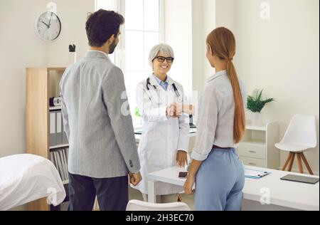 Young couple shaking hands with smiling family practitioner or pregnancy specialist Stock Photo