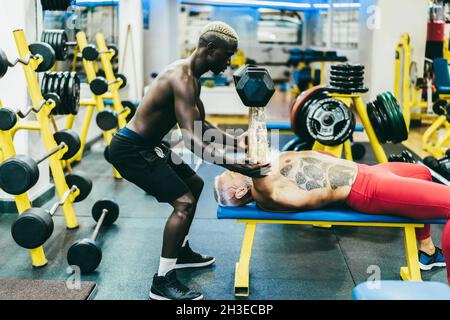 Young trainer and senior man doing workout sessions inside gym club - Focus on african man face Stock Photo