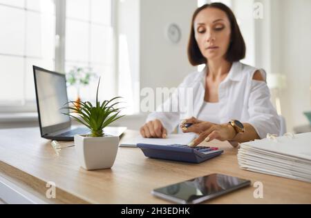 Woman checks finances, calculates bills or taxes using online banking services at home or in office. Stock Photo