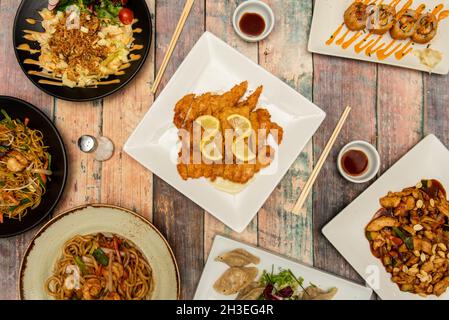 food dishes cooked in a Chinese restaurant. Chicken in batter with lemon sauce, noodles with shrimp and sautéed vegetables, steamed gyozas, uramaki su Stock Photo