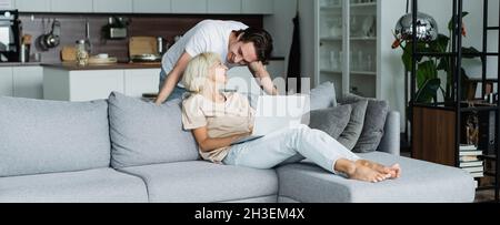 happy man looking at blonde girlfriend working from home with laptop, banner Stock Photo