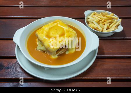 Francesinha is a Portuguese sandwich, made with bread, ham, linguica, sausage, steak, and covered with, cheese and beer sauce. Close up Stock Photo