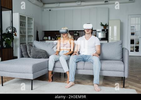 shocked couple in vr headsets sitting on grey couch Stock Photo