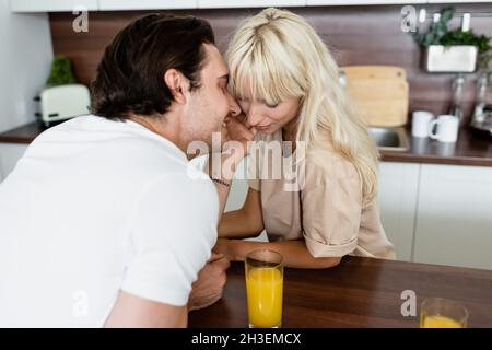 tattooed man touching face of blonde girlfriend near glasses with orange juice Stock Photo