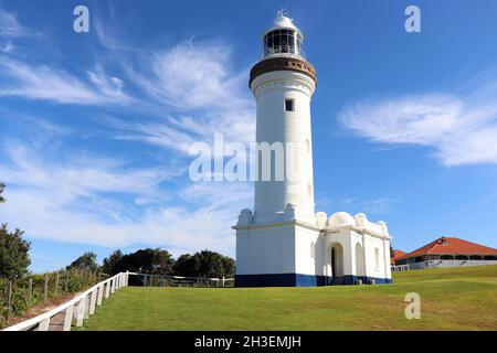 A gorgeous white lighthouse sitting on green grass offset by a blue sky with whispy whimsical clouds Stock Photo