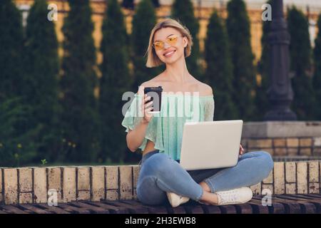 Full size photo of lovely millennial blond lady drink coffee write laptop wear green blouse spectacles outsite in park Stock Photo