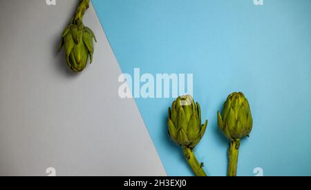 Three artichokes on grey and blue background Stock Photo