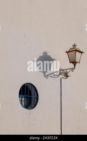 Street lamp and shadow with small round blue window on white wall Stock Photo