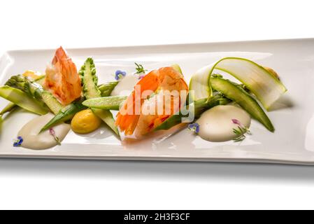 Shrimps with asparagus and zucchini, gourmet recipe in white dish isolated on white, copy space Stock Photo