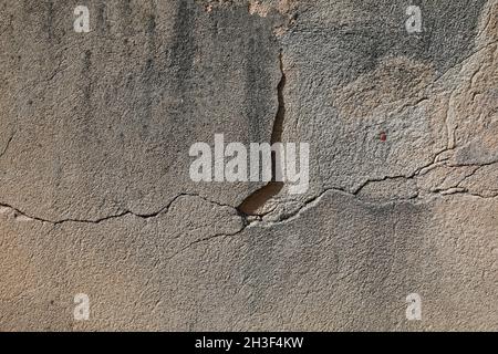 The old brick wall was once plastered. Currently, the surface of the wall is cracking and there are visible plaster defects. Stock Photo