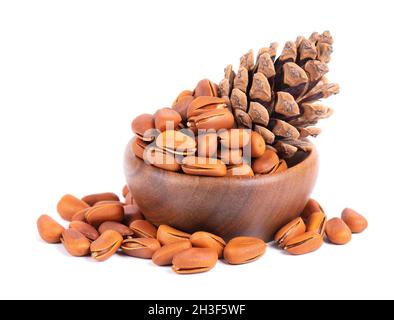 Pine nuts in wooden bowl, isolated on white background. Pine cones and heap of roasted pine nuts in shells. Stock Photo