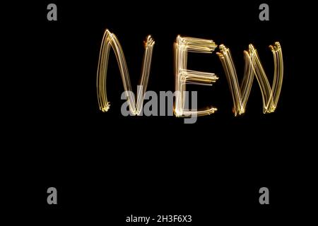 The word 'new' written against black background with long exposure yellow light. Happy new year concept photo. Stock Photo