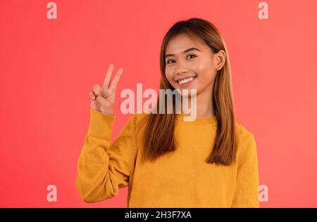 Young attractive asian girl smiling with peace sign in studio Stock Photo