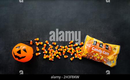 Moscow, Russia, September 2021: Plastic pumpkin basket, candy corn Brachs spilled out of the pack. Halloween sweets. Copy space. Stock Photo