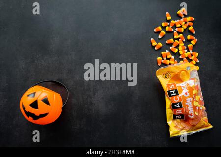 Moscow, Russia, September 2021: Plastic pumpkin basket, candy corn Brachs spilled out of the pack. Halloween sweets. Copy space. Stock Photo
