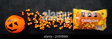 Moscow, Russia, September 2021: Banner with plastic pumpkin basket, candy corn Brachs spilled out of the pack. Halloween sweets. Copy space. Stock Photo